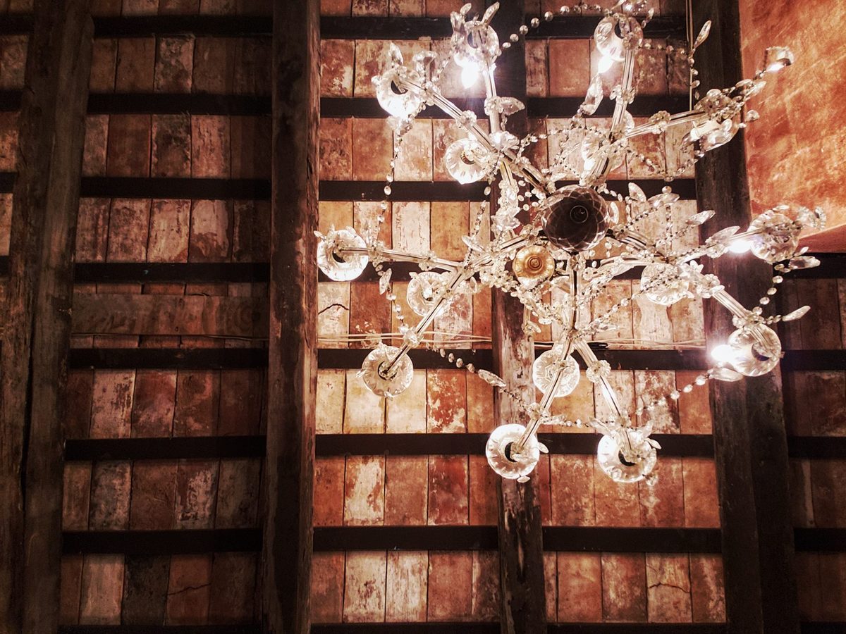 A crystal chandelier hanging beneath aged wooden ceiling beams.