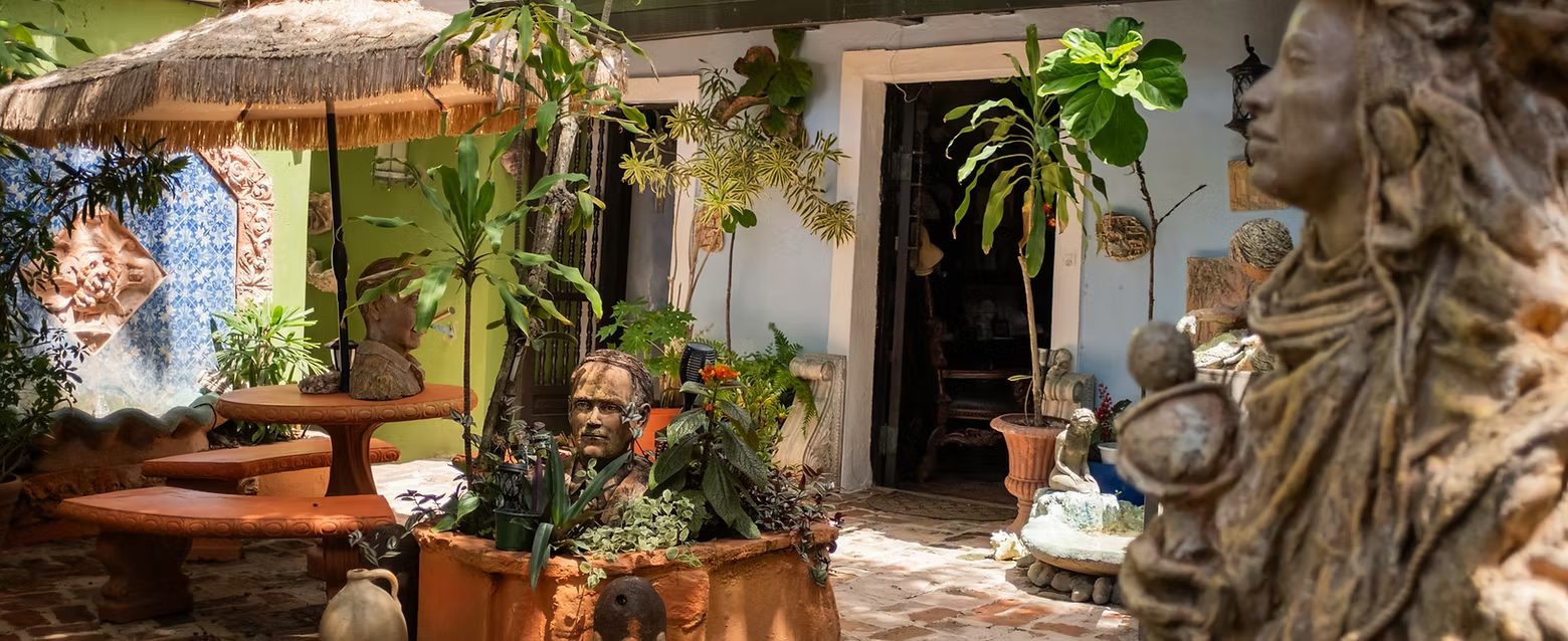 A tropical courtyard at The Gallery Inn with sculptures, terracotta, and lush plants in dappled light.