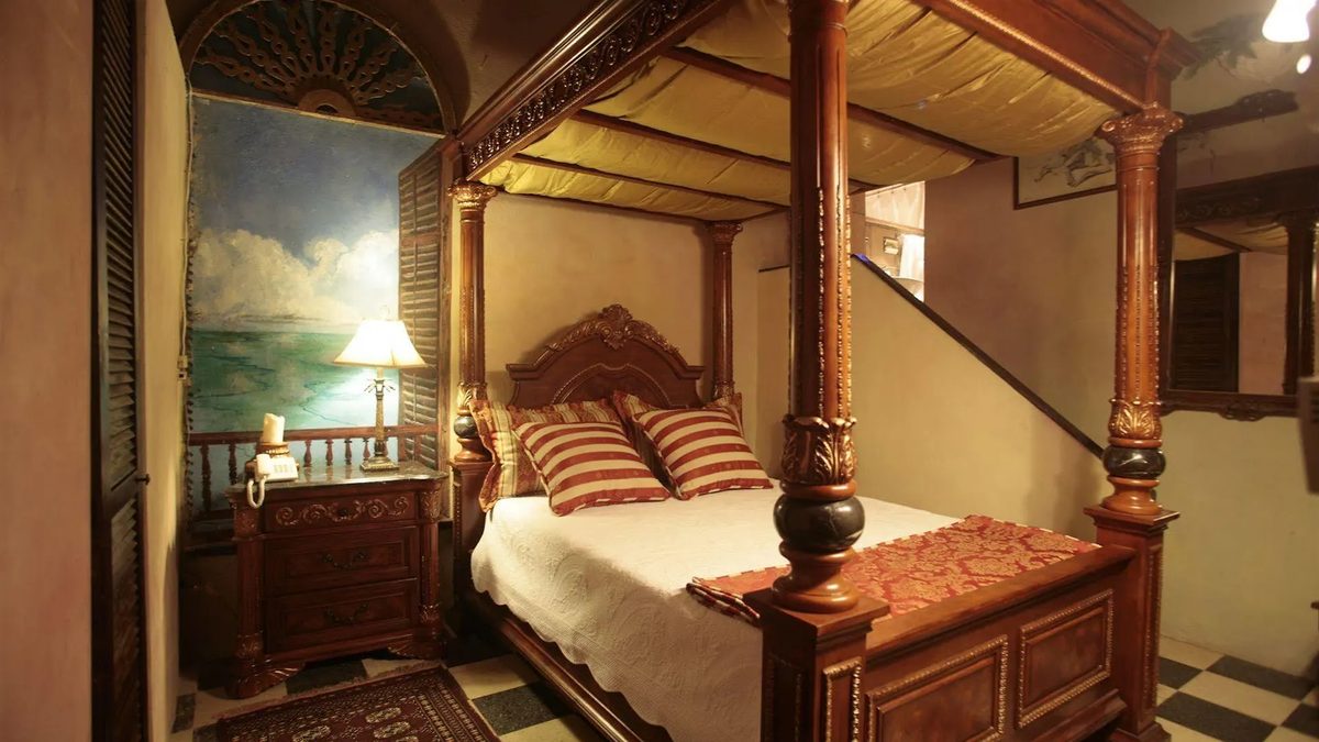 An Artist Student Room at The Gallery Inn - a carved wood four-poster bed, a painted seascape mural, louvered shutters, and a checkered floor.