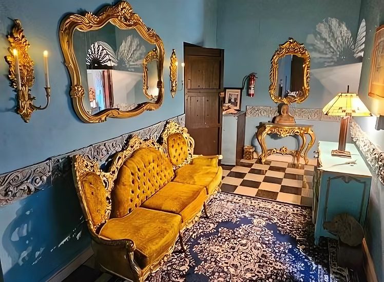 A sitting area in the Balcony Suite with a gold velvet antique sofa and gilded mirrors.