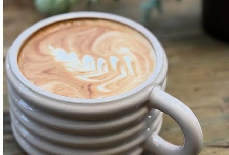 A café con leche with latte art in a ribbed ceramic cup on a rustic wood table at Café Galería.