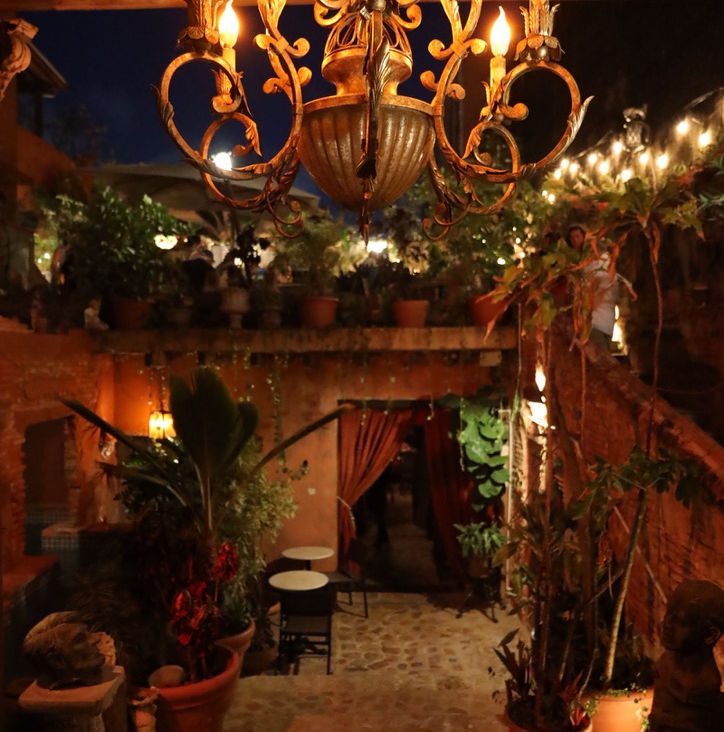 A lantern-lit garden at The Cannon Club at night - a brass chandelier, tropical plants, terracotta walls, and café lights.
