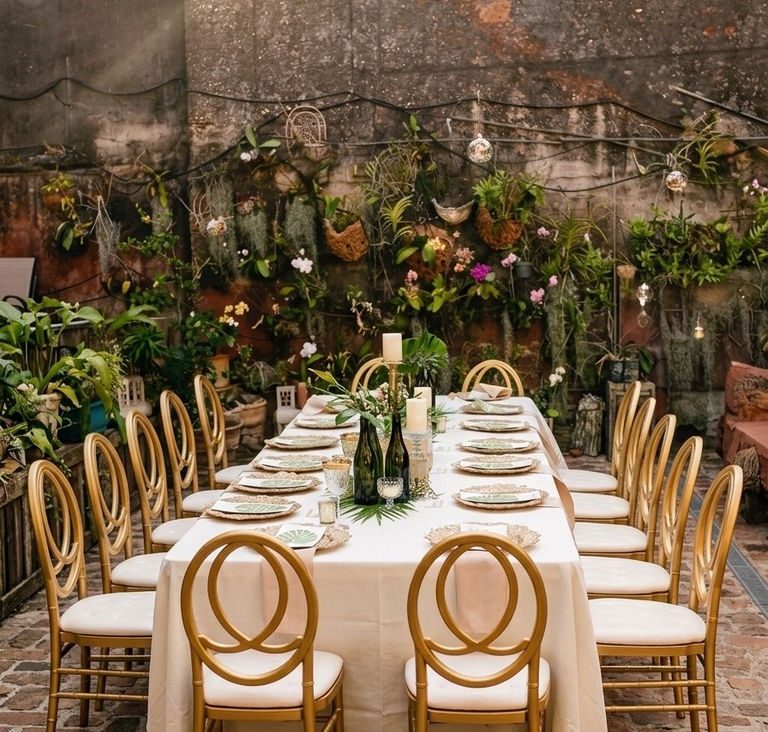 A long candlelit table set for a private dinner at The Cannon Club - gold chairs, white linen, and a plant-covered wall under café lights.