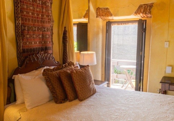 A Colonial Room at The Gallery Inn - golden walls, a carved headboard, and shutter doors open to a balcony.
