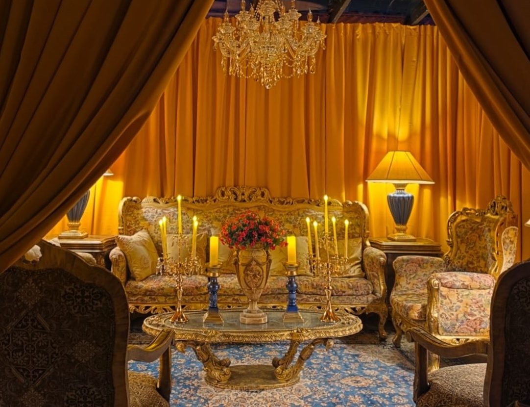 The Double Suite's sitting room at The Gallery Inn - gold drapery and a crystal chandelier over a carved gilded sofa and armchairs, candelabras lit on an ornate table.