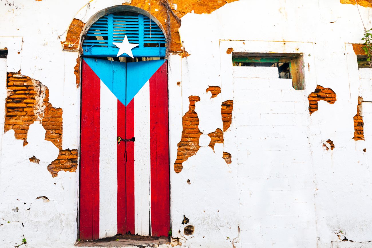 A weathered door in Old San Juan painted with the Puerto Rican flag, set in cracked plaster and exposed brick.