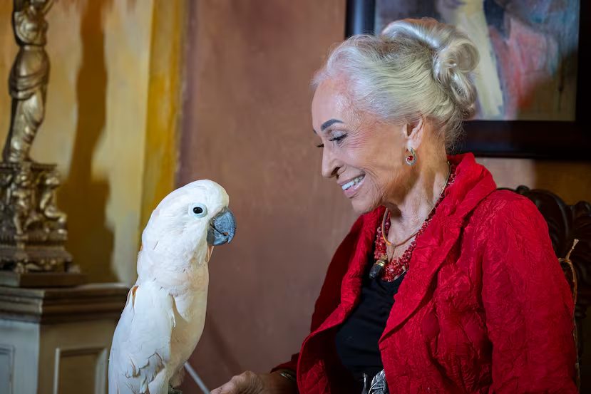Artist Jan D'Esopo in a red jacket beside a white cockatoo inside The Gallery Inn.
