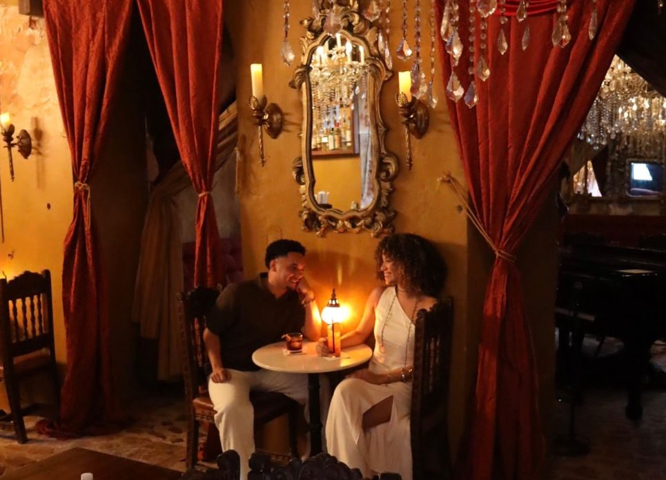 A candlelit table at The Cannon Club, with red velvet, gilded mirrors, and a grand piano beyond.