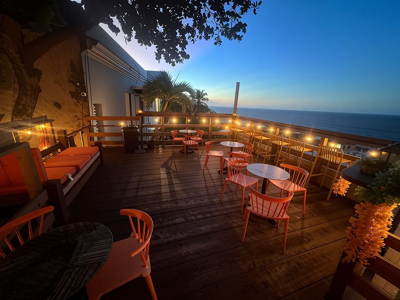 Nico Bar at dusk - a rooftop deck strung with café lights and orange chairs, open to the Atlantic Ocean and the twilight sky.