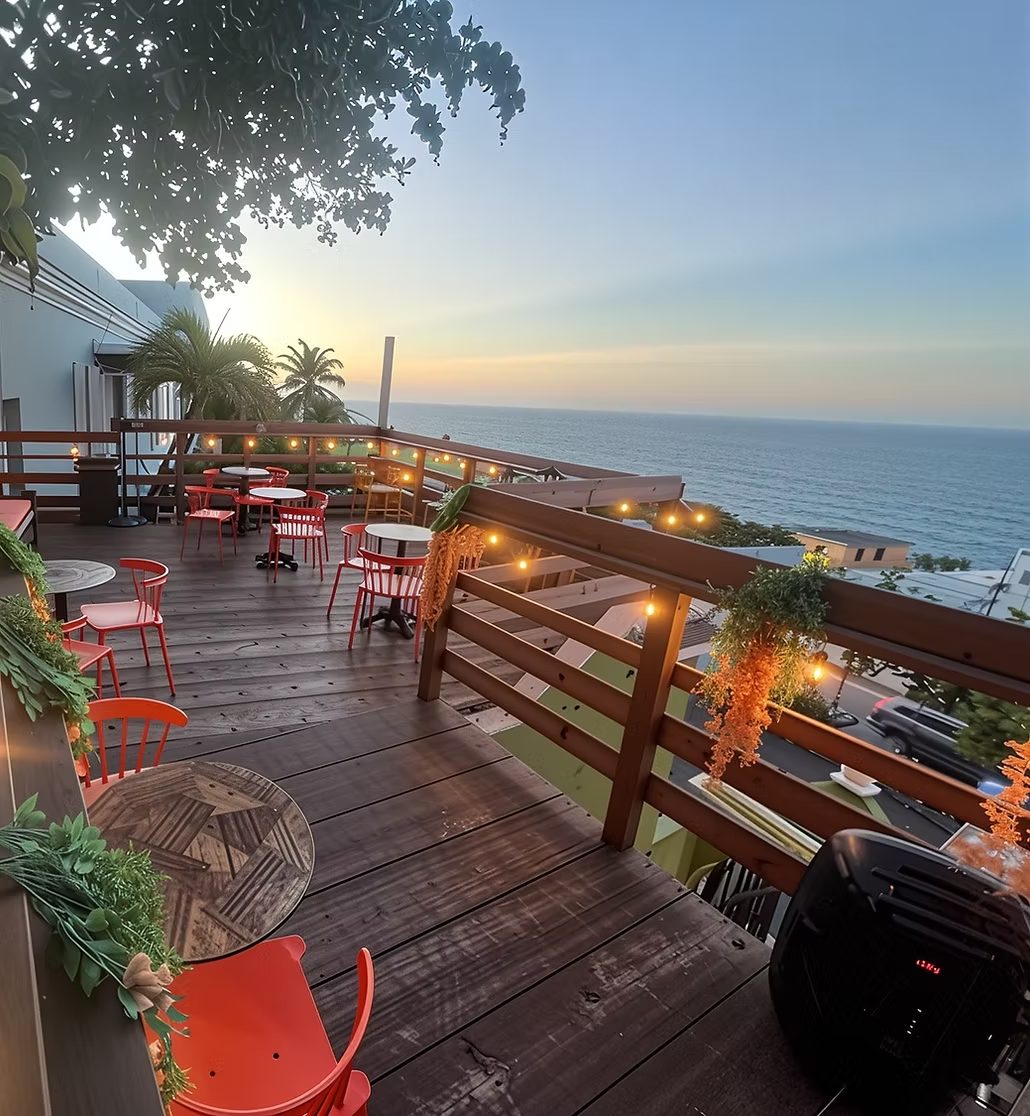Nico Bar at golden hour - a rooftop deck with coral chairs, café lights along the rail, palms, and the Atlantic stretching to the sunset horizon.