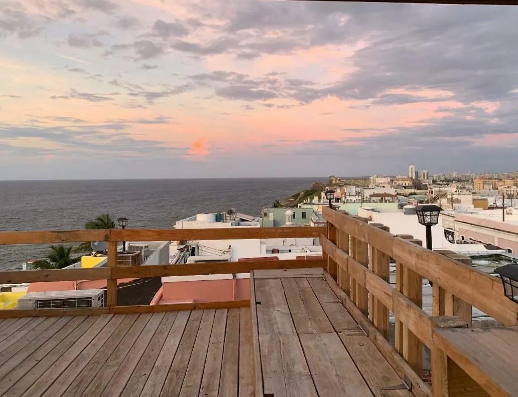 The Gallery Inn's private roofdeck - a timber deck and railing high above Old San Juan, open to the rooftops, harbor, and Atlantic at sunset.