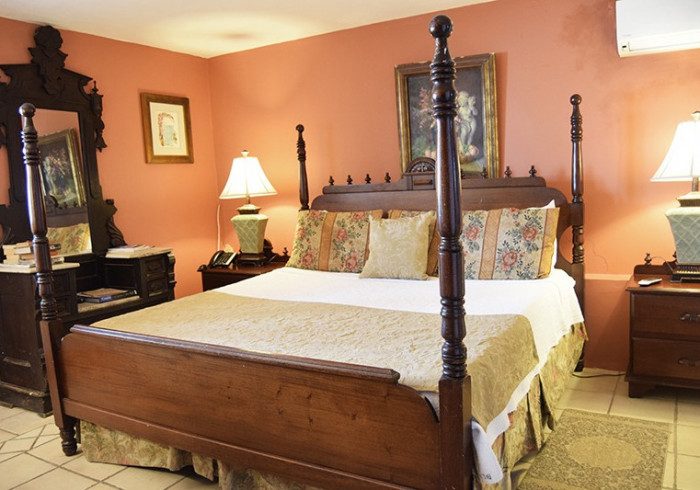 A Top Suite at The Gallery Inn - a grand carved dark-wood four-poster bed against terracotta walls, an ornate antique mirror, and framed art.